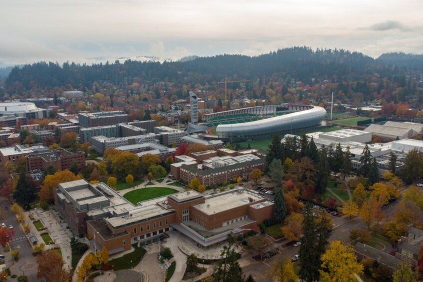 An aerial view of a university campus with buildings, a large stadium, and surrounding autumn foliage. 3