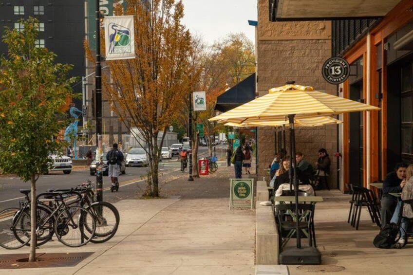 A sidewalk with bicycles, a street, a restaurant with outdoor seating, and autumn trees. 2