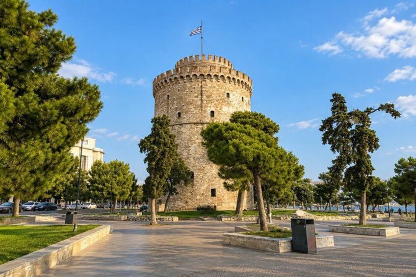 A historic stone tower with a flag, surrounded by trees and a paved walkway. 4