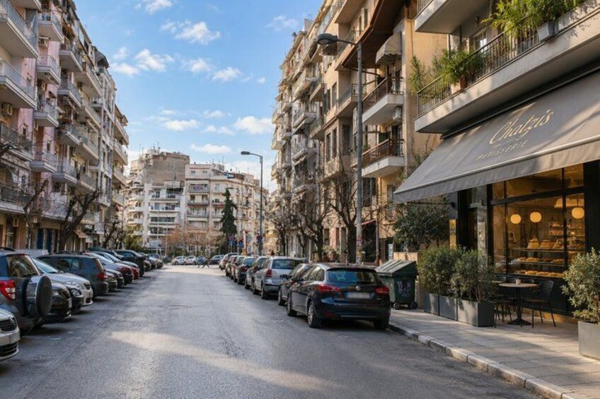 A street lined with parked cars, multi-story residential buildings, and a restaurant with outdoor seating. 5
