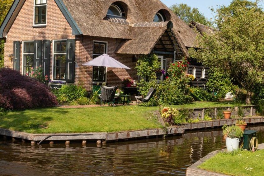 A house with a thatched roof, a pond, and a garden with flowers and plants. 4