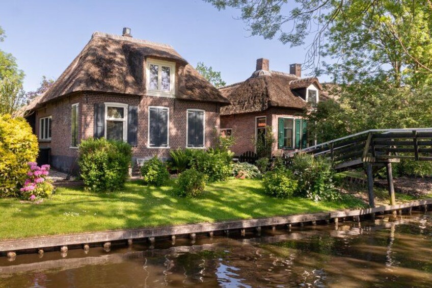 A traditional brick house with a thatched roof, surrounded by lush greenery and a small pond. 5