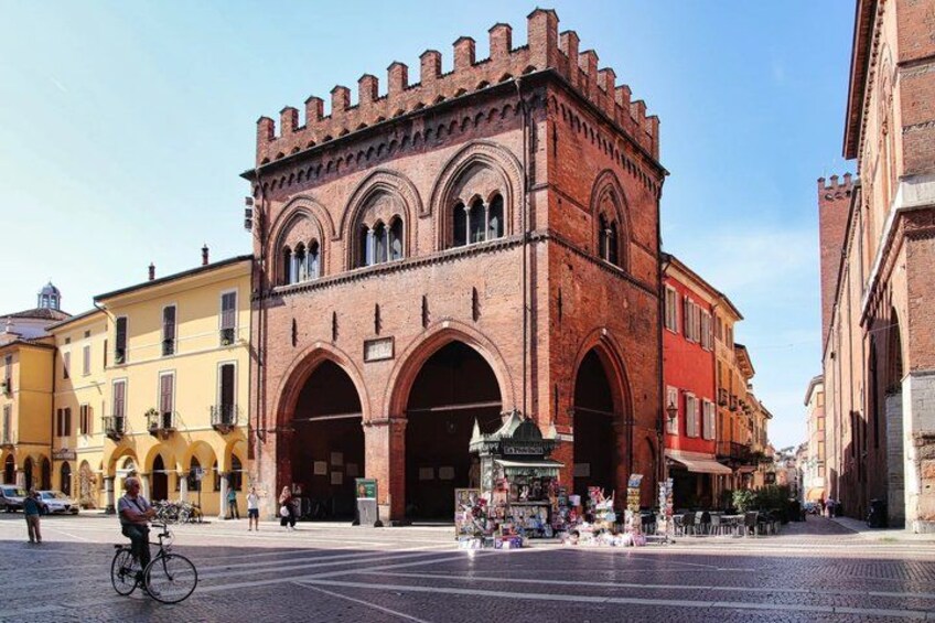 A historic red brick building with arched entrances, a cyclist, and a street market. 4