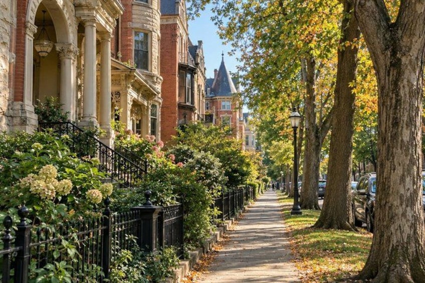 A tree-lined street with historic buildings, a sidewalk, and a clear sky. 2