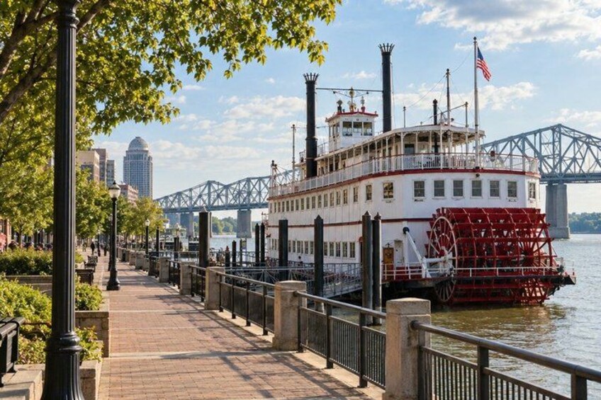 A riverboat docked at a pier with a bridge in the background. 1