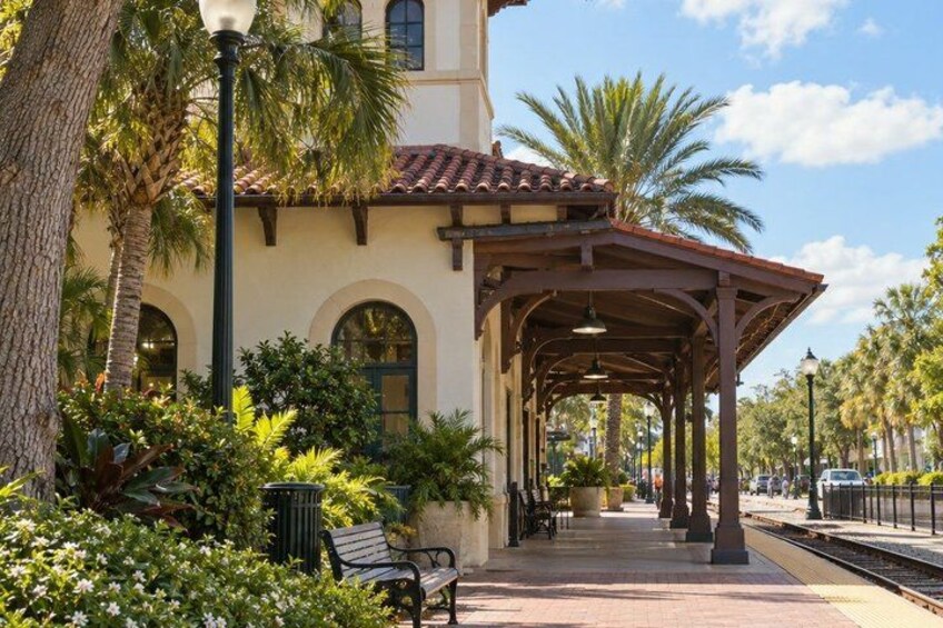 A covered outdoor area with a bench, palm trees, and a building with arched windows. 4