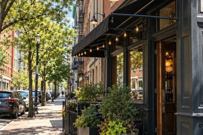 A street with parked cars, trees, and a building with outdoor seating. 3