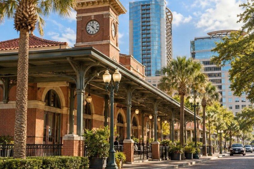 A historic building with a clock tower, a covered walkway, palm trees, and modern high-rise buildings in the background. 4