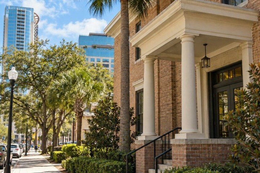 A brick building with a porch, palm trees, and a street with cars. 2