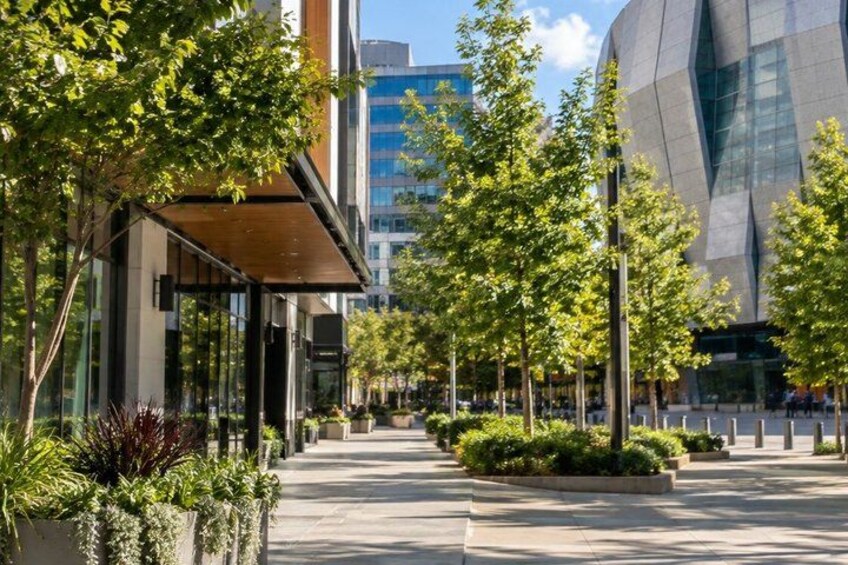 A modern urban street with trees, a building with a unique geometric facade, and a clear sky. 4