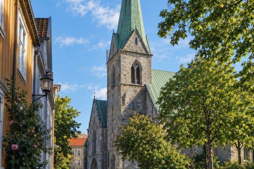 A church with a green roof and a tall tower, surrounded by trees and buildings. 4