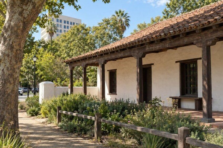 A historic building with a tiled roof, surrounded by greenery and a wooden fence. 1