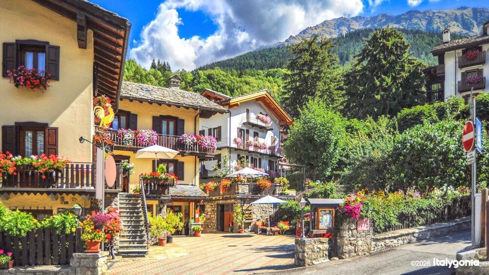 A picturesque village street with colorful flower boxes, traditional buildings, and a mountain backdrop. 1