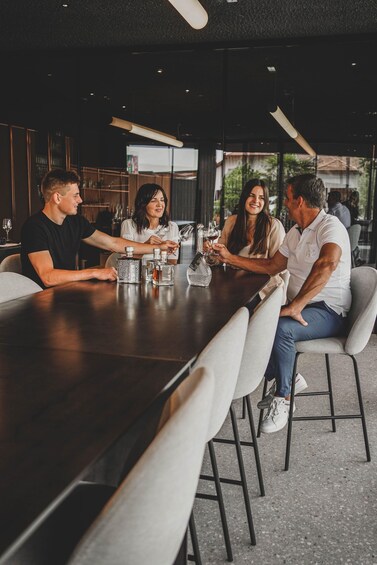 A group of people sitting around a long table in a modern indoor setting with glassware and bottles. 3