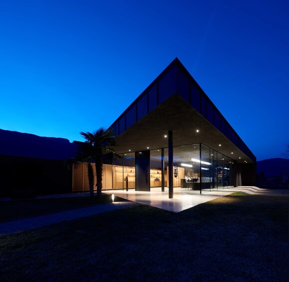 A modern building with a triangular roof and glass facade at dusk. 1