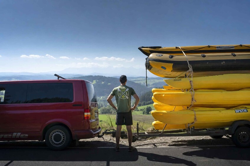 A person standing next to a red van with kayaks stacked on the right. 2
