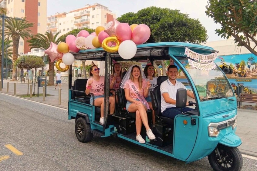 A teal tuk-tuk decorated with balloons and a banner, with passengers in casual attire. 1