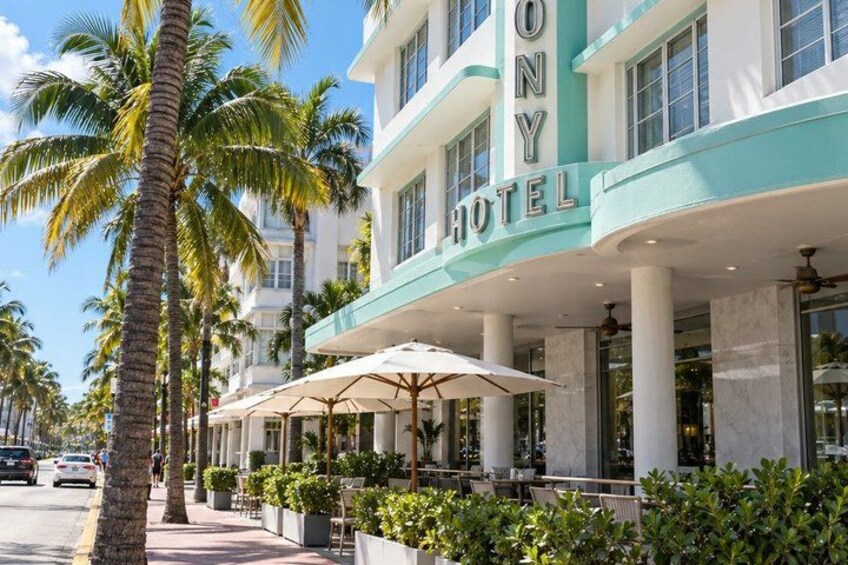 A hotel with a teal facade, palm trees, and outdoor seating with umbrellas. 5