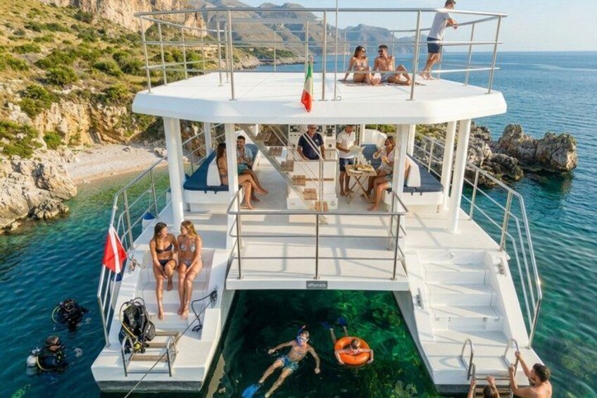 A boat with people on deck, a clear blue sea, rocky coastline, and a flag. 2