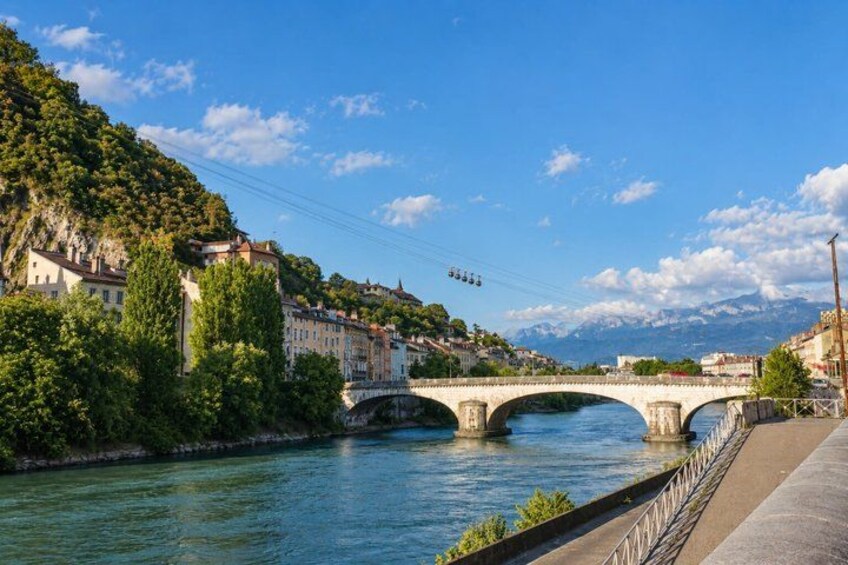 A river with a stone bridge, buildings on a hillside, and mountains in the background. 3