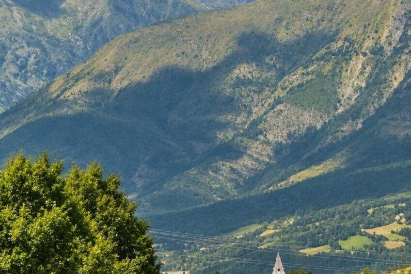 A mountainous landscape with a church spire and dense greenery. 2