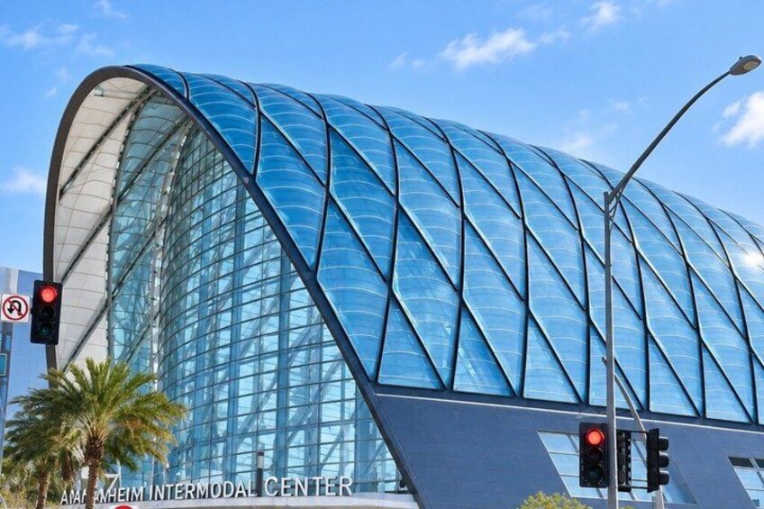A modern glass building with a curved roof, traffic lights, and palm trees. 2