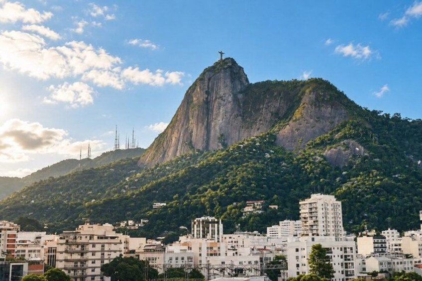 A cityscape with a prominent mountain, a cross on top, and several buildings. 4