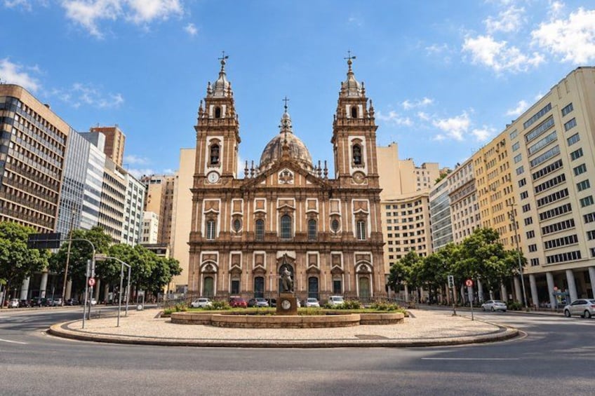 A historic church with two towers, surrounded by modern buildings and a roundabout. 2