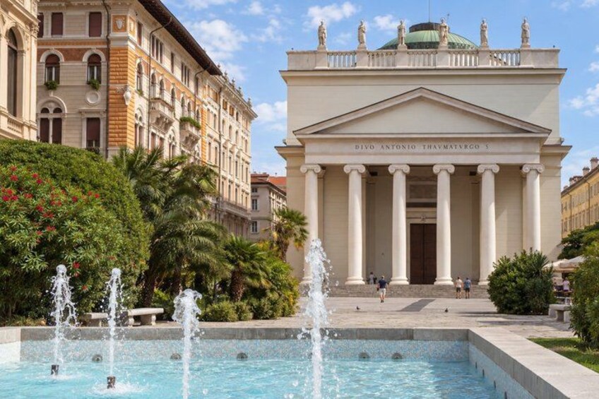 A classical building with columns, a fountain, and lush greenery. 3