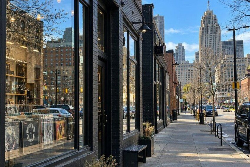 A city street with storefronts, parked cars, and a clear sky. 2