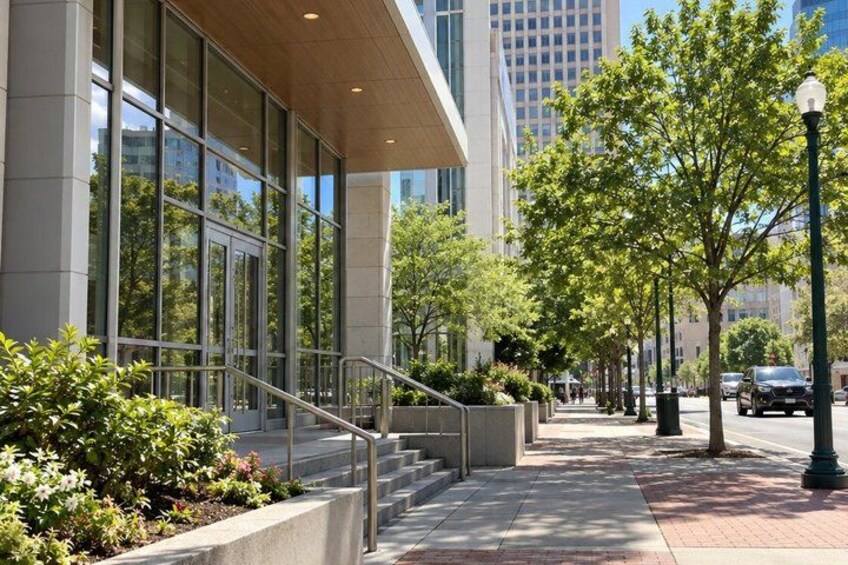 A modern building with large windows, a sidewalk, trees, and a street with cars. 4