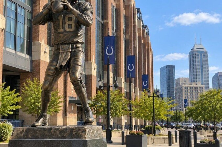 A bronze statue of a football player in a cityscape with tall buildings and a clear sky. 2