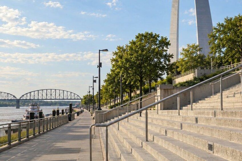 A waterfront promenade with a bridge, a tall monument, and a boat. 4