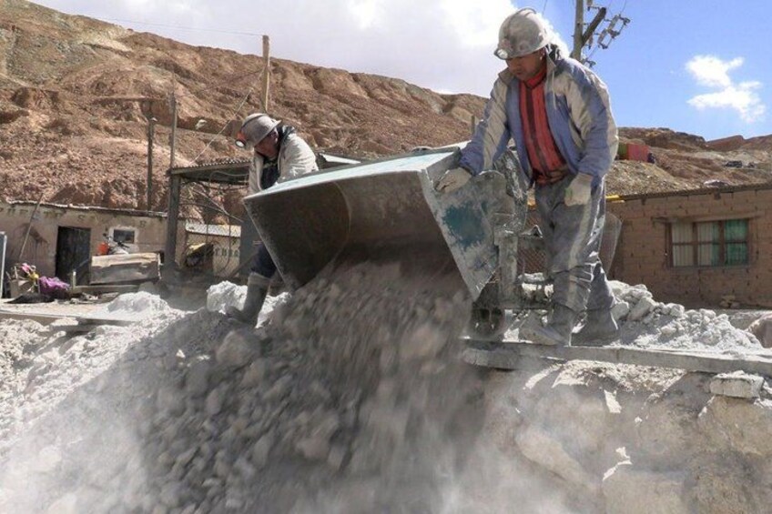 A person operating a concrete mixer in an industrial setting with a pile of concrete and a building in the background. 4