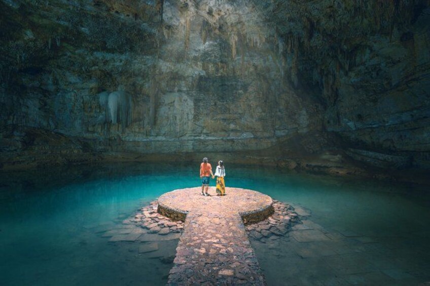 A person standing on a circular stone platform in a cave with a pool of water. 1