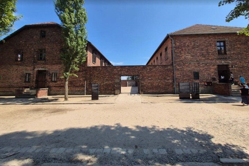 A brick building with a central entrance, surrounded by a gravel area and trees. 2