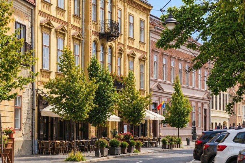 A street with historic buildings, outdoor seating, and parked cars. 5