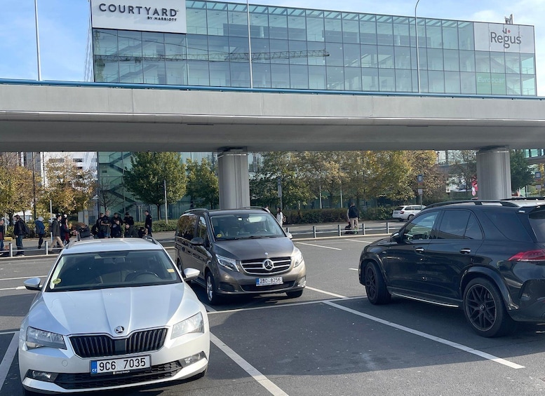 A parking lot with several cars, a modern building with glass facade, and a pedestrian walkway. 4