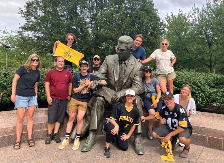 A group of people posing with a statue of a man in a suit and a yellow sign. 2