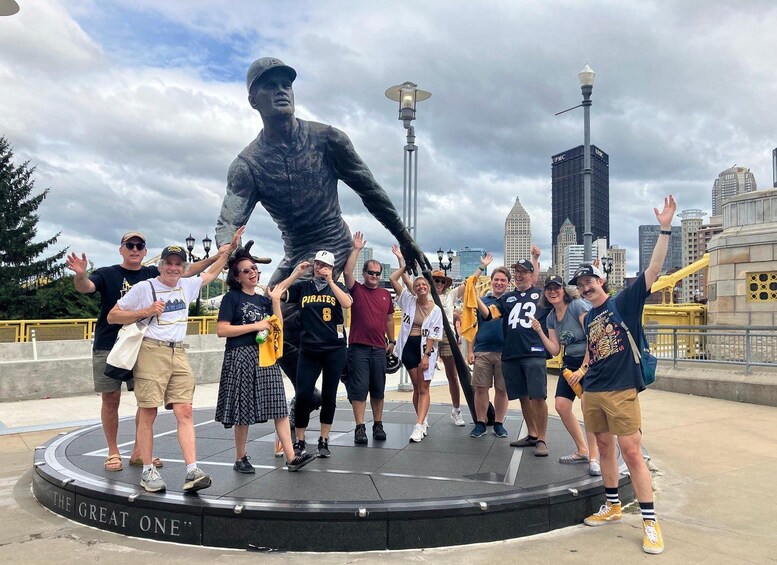 A group of people posing with a large statue of a baseball player in a city setting. 1