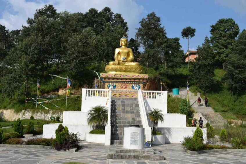 Une grande statue de Bouddha en or, posée sur un piédestal auquel on accède par un escalier, entourée de verdure et avec quelques personnes qui se promènent en arrière-plan. 2