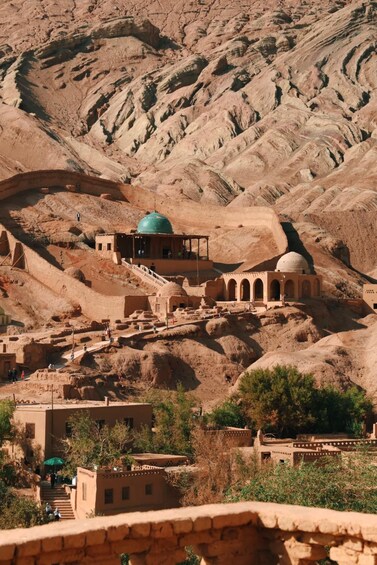 Un paysage montagneux caractérisé par une architecture traditionnelle, notamment une mosquée dotée d’un dôme vert et de structures en arc. 5