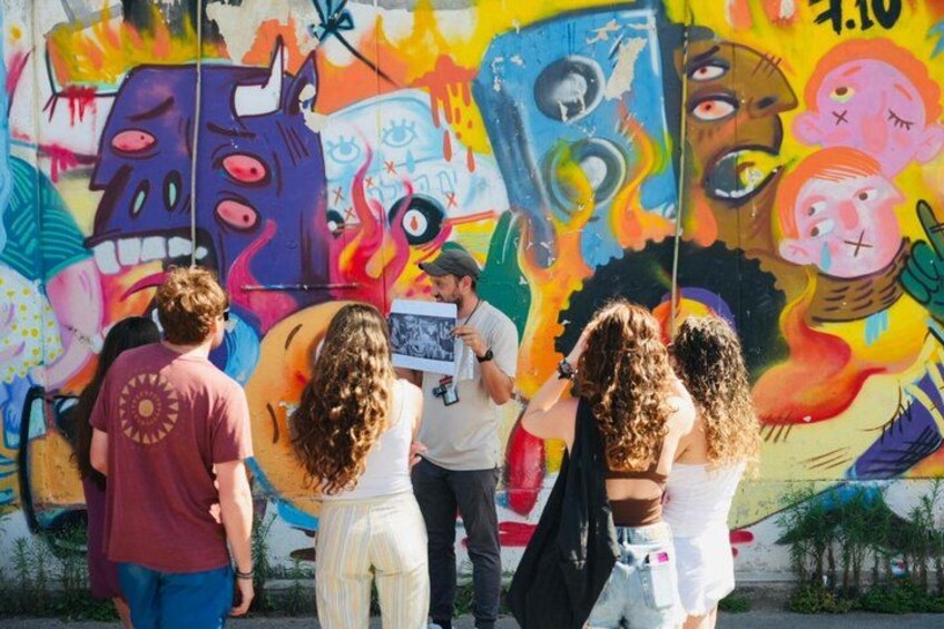 A group of people observing a colorful mural with various abstract figures and designs. 1