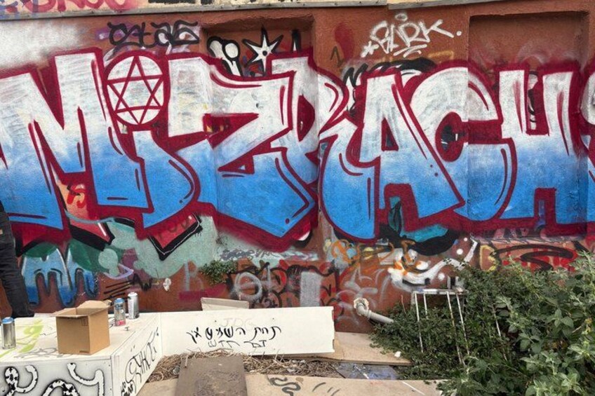A wall with graffiti, including large blue letters and various tags. 5