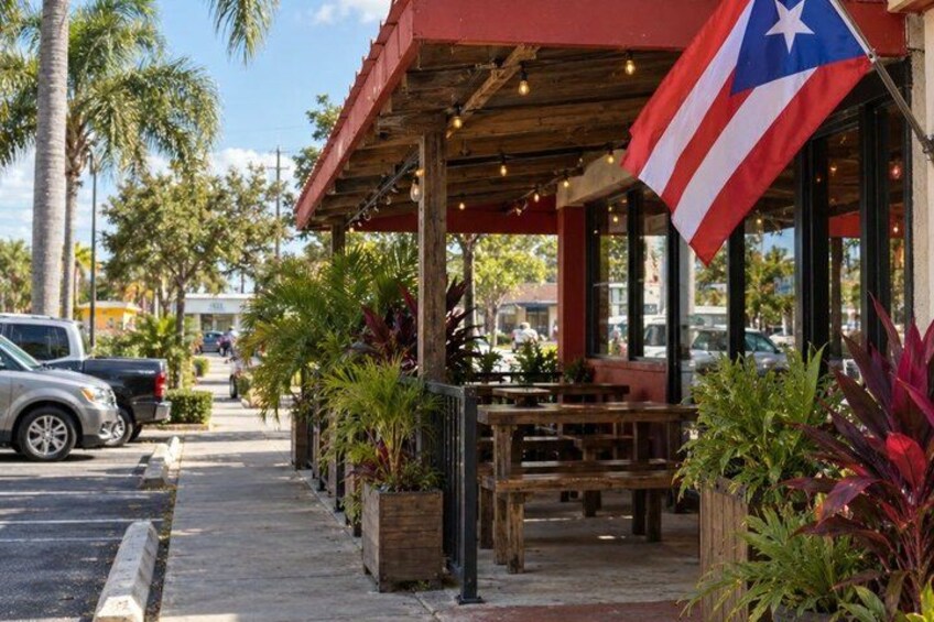 A restaurant with outdoor seating, a flag, and palm trees. 3