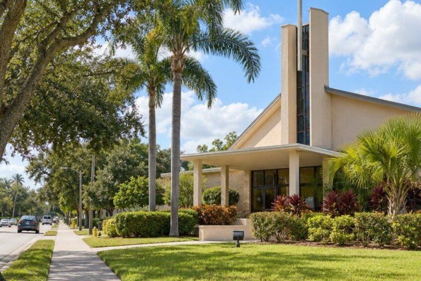 A modern building with a flat roof, surrounded by well-maintained grass and palm trees. 4