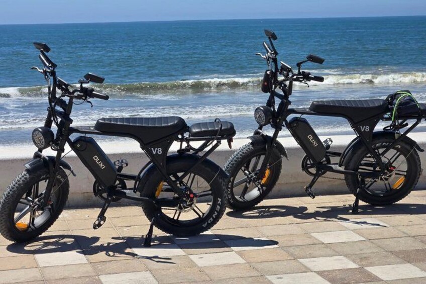 Three electric scooters parked on a tiled surface by the ocean. 4