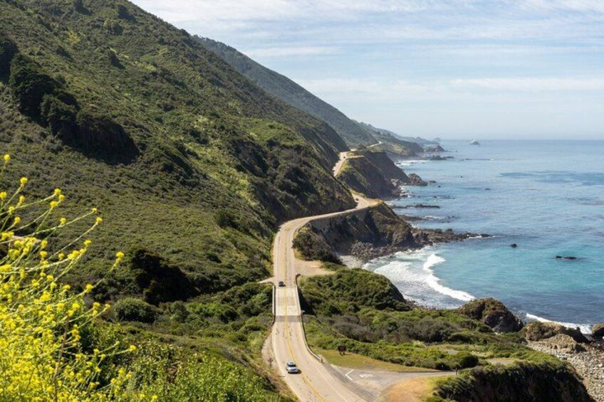 A winding coastal road with a vehicle, surrounded by lush green hills and the ocean. 5