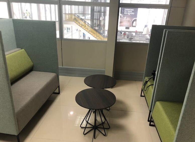 A modern office space with a gray sofa, two round tables, and green and gray cubicle partitions. 3