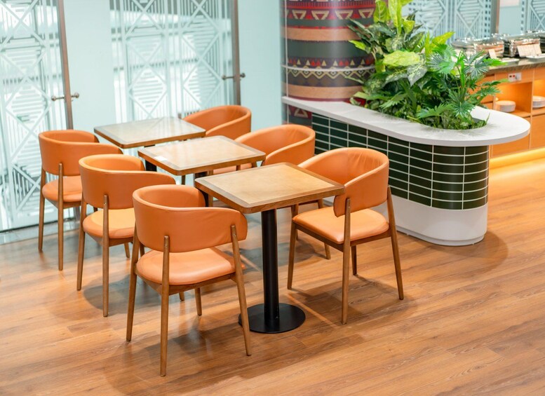 A modern cafe interior with wooden tables and orange chairs, a decorative plant, and a patterned wall. 5
